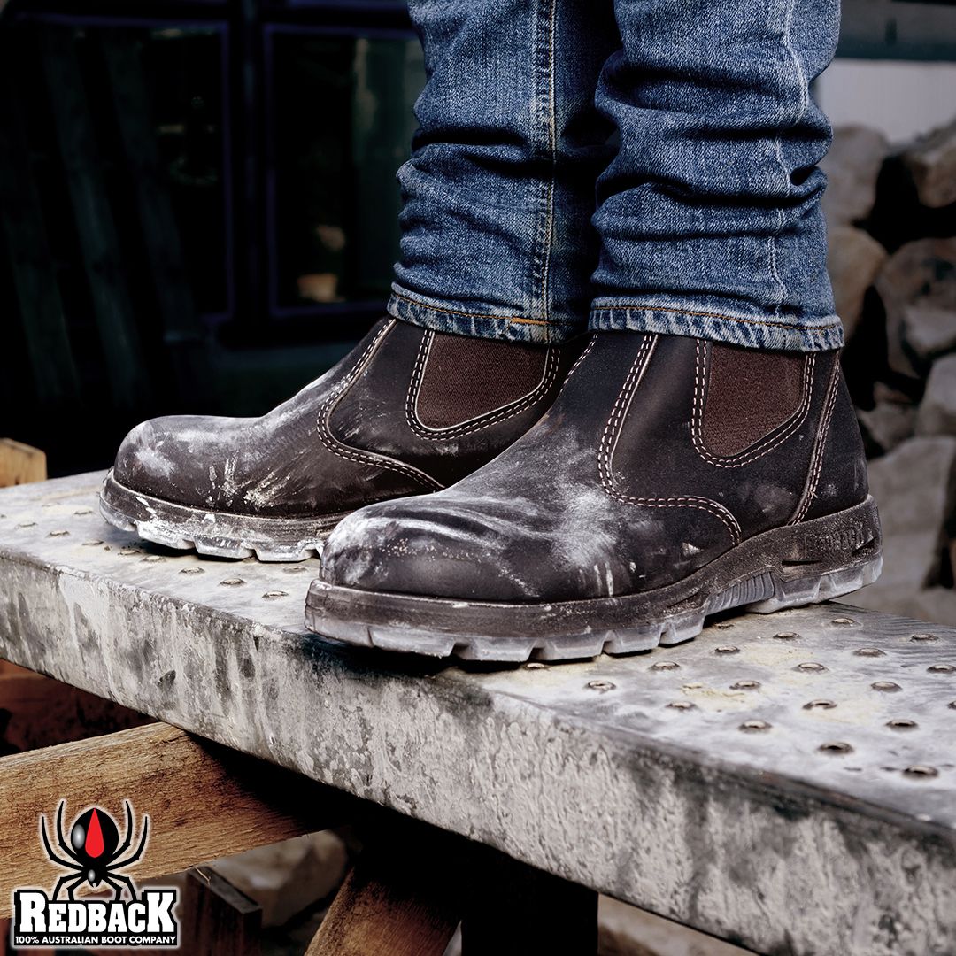 Person wearing dark work boots and blue jeans standing on a wooden platform with Redback logo visible.